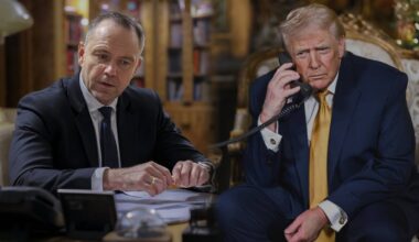 Dw&oacute;ch mężczyzn siedzi przy stole, jeden rozmawia przez telefon, drugi patrzy w bok.