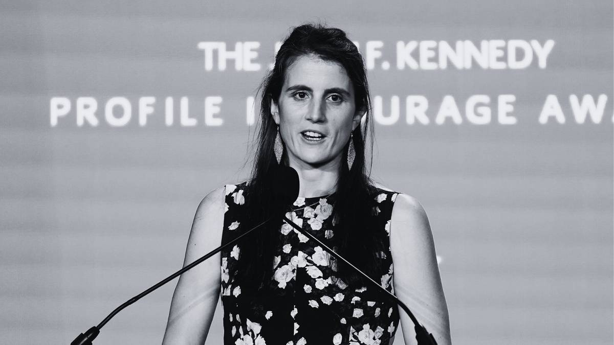 Kobieta w sukience w kwiaty przemawia do mikrofonu na tle napisu "THE J.F. KENNEDY PROFILE IN COURAGE AWARD".