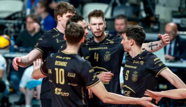 Grupa siatkarzy w czarnych strojach sportowych świętuje razem na boisku.