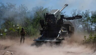 Działon armaty polowej w akcji, otoczony chmurą pyłu i dymu, z widocznym żołnierzem w pobliżu.