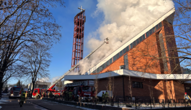 Strażacy gaszą pożar kościoła, używając podnośnika i węży strażackich. Z dachu budowli wydobywają się kłęby dymu.