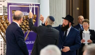 Uczestnicy uroczystości Chanuka w Sejmie, wśr&oacute;d nich mężczyzna z jarmułką zapalający świecę przy menory.