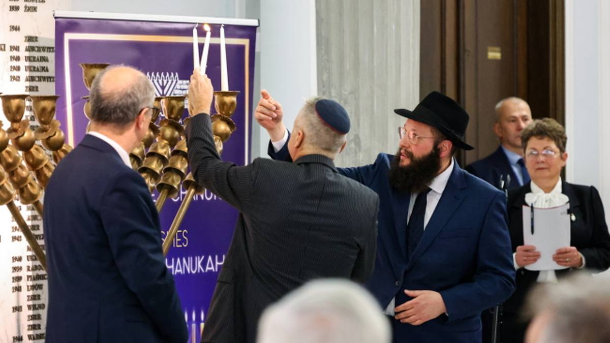 Uczestnicy uroczystości Chanuka w Sejmie, wśr&oacute;d nich mężczyzna z jarmułką zapalający świecę przy menory.