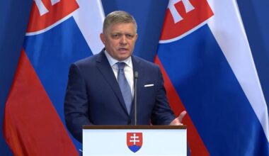 Premier Słowacji Robert Fico przemawia za m&oacute;wnicą z herbem Słowacji, w tle flagi Słowacji.