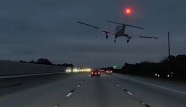 Mały samolot leci nisko nad autostradą podczas zmierzchu, z czerwonym światłem na ogonie. Na drodze widać kilka samochodów.