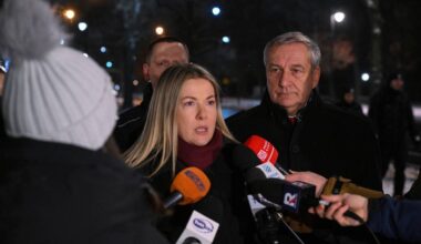 Kobieta w białej czapce z pomponem i szaliku przemawia do dziennikarzy, za nią stoi mężczyzna w garniturze.