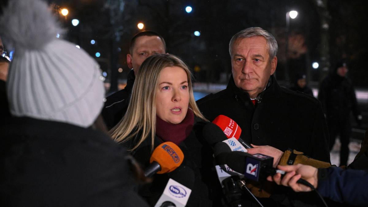 Kobieta w białej czapce z pomponem i szaliku przemawia do dziennikarzy, za nią stoi mężczyzna w garniturze.