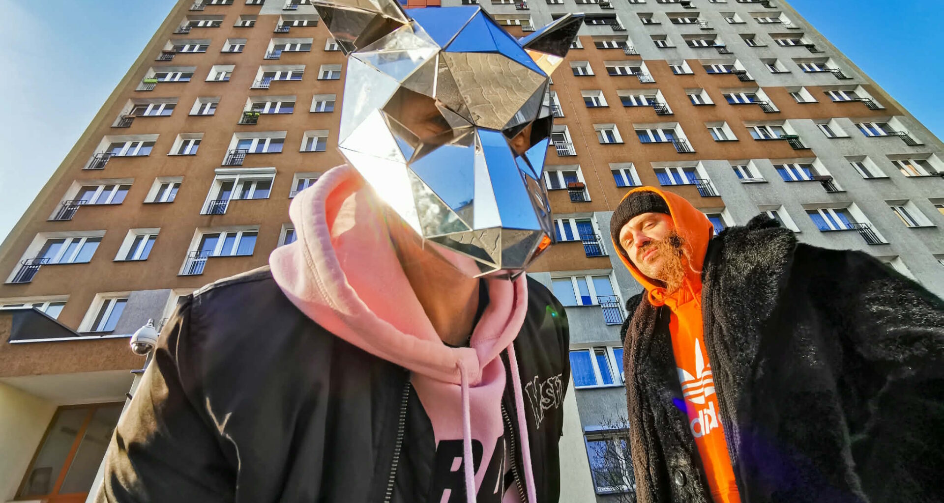 Dwóch mężczyzn, jeden w masce, w tle wieżowiec