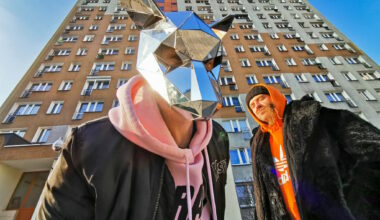 Dwóch mężczyzn, jeden w masce, w tle wieżowiec