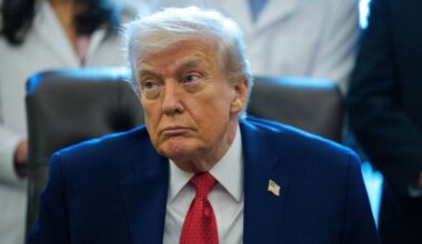 Donald Trump w garniturze i czerwonym krawacie, patrzący w bok z poważnym wyrazem twarzy.