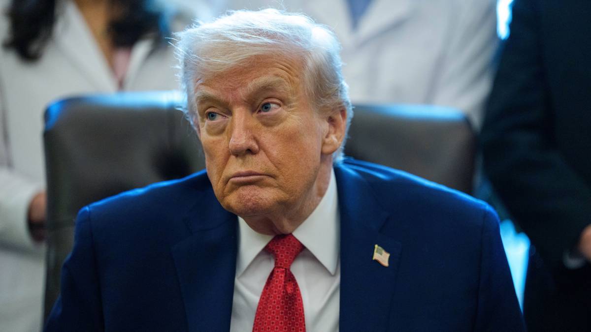 Donald Trump w garniturze i czerwonym krawacie, patrzący w bok z poważnym wyrazem twarzy.