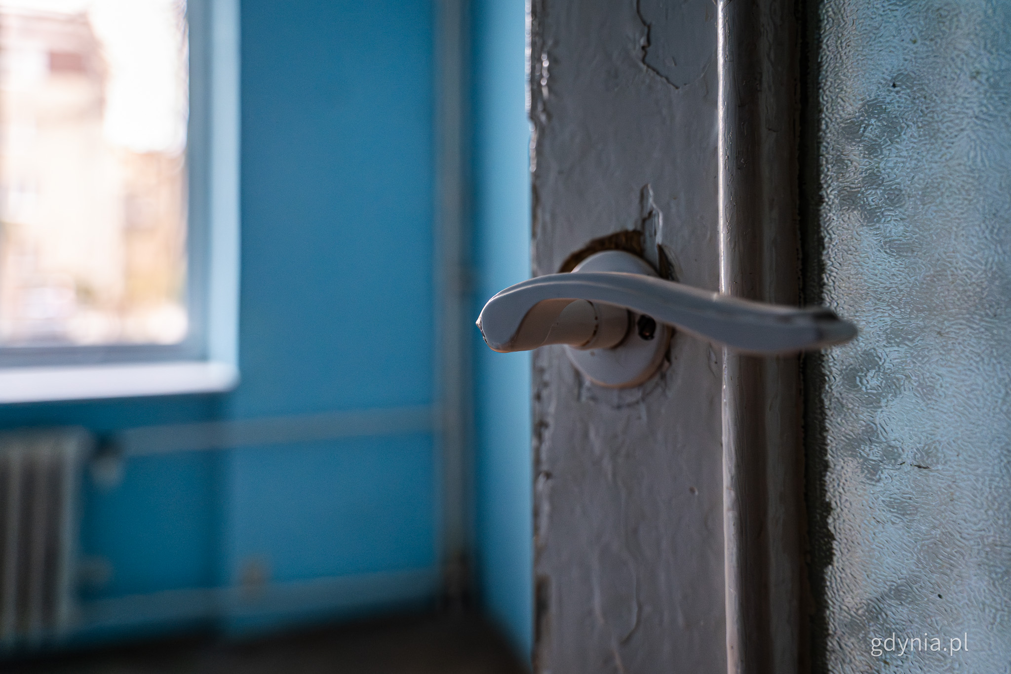Puste mieszkanie, niebieskie ściany, widoczna biała klamka od drzwi i okno
