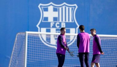 Trzech piłkarzy FC Barcelony w strojach treningowych stoi przed bramką na boisku treningowym.