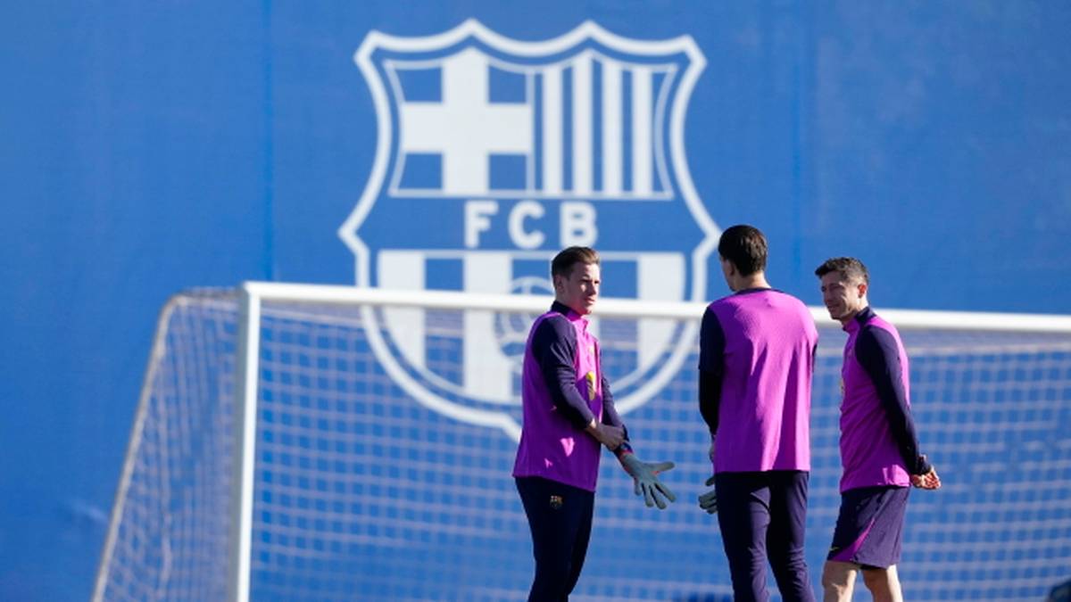 Trzech piłkarzy FC Barcelony w strojach treningowych stoi przed bramką na boisku treningowym.