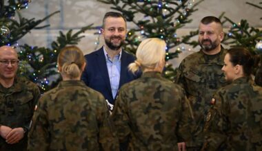 Szef MON wraz z żołnierzami w świątecznej atmosferze, z choinkami w tle.