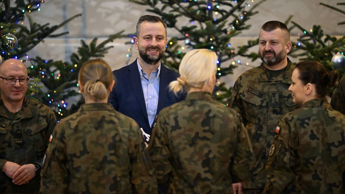 Szef MON wraz z żołnierzami w świątecznej atmosferze, z choinkami w tle.