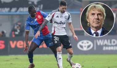 Dwóch piłkarzy na boisku podczas meczu piłki nożnej. Jeden z nich, w białej koszulce z numerem 30, prowadzi piłkę, podczas gdy drugi, w niebiesko-czerwonej koszulce, próbuje go zatrzymać. W prawym górnym rogu zdjęcia znajduje się portret starszego mężczyzny w garniturze.