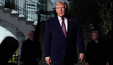 Donald Trump w garniturze i krawacie wychodzi po schodach, w tle dwie postacie w ciemnych ubraniach.