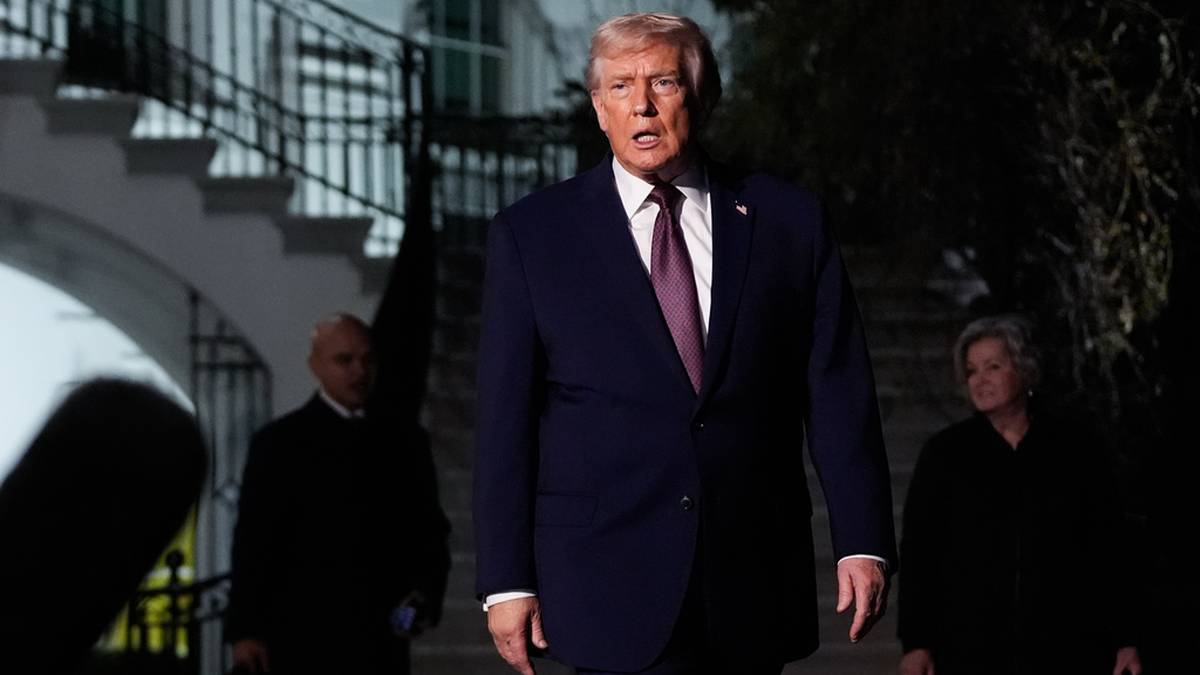 Donald Trump w garniturze i krawacie wychodzi po schodach, w tle dwie postacie w ciemnych ubraniach.