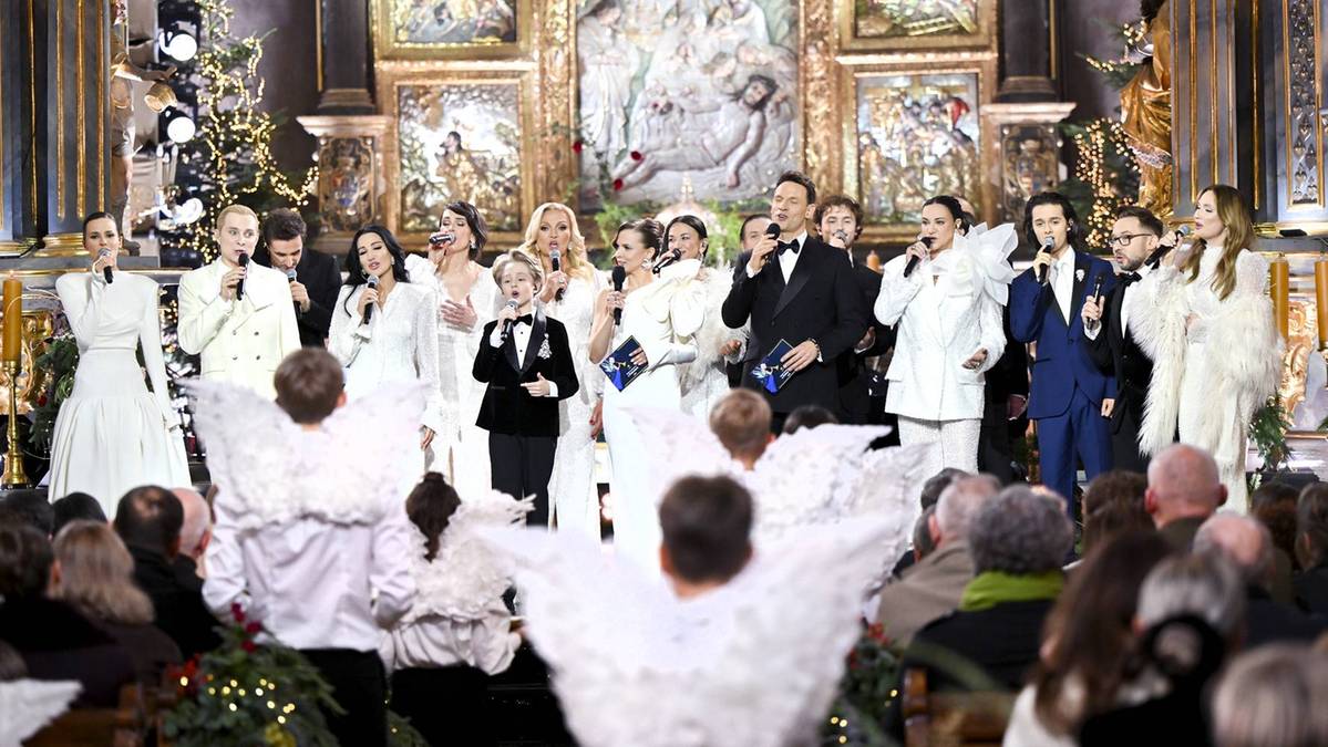 Artyści występują na scenie w kościele podczas koncertu kolęd, w tłumie widz&oacute;w.