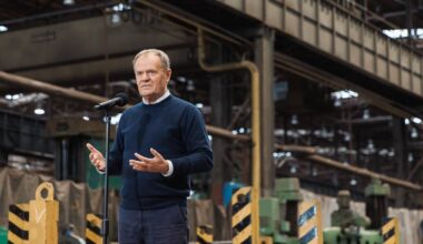Premier Donald Tusk przemawia w industrialnym otoczeniu.