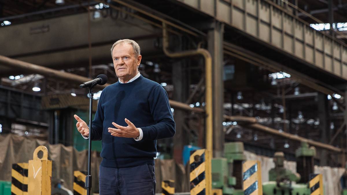 Premier Donald Tusk przemawia w industrialnym otoczeniu.