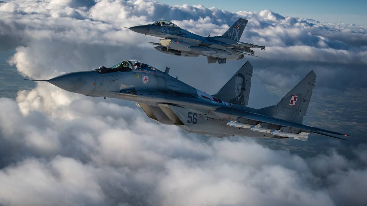Dwa myśliwce, jeden MIG-29 i jeden F-16, lecące nad chmurami.