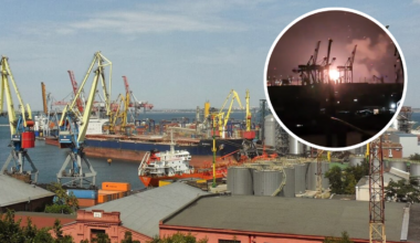 Widok na port morski z licznymi dźwigami, statkami i budynkami przemysłowymi. W prawym g&oacute;rnym rogu okrągłe okno z widokiem na nocny atak z eksplozjami i dymem w tle portu.