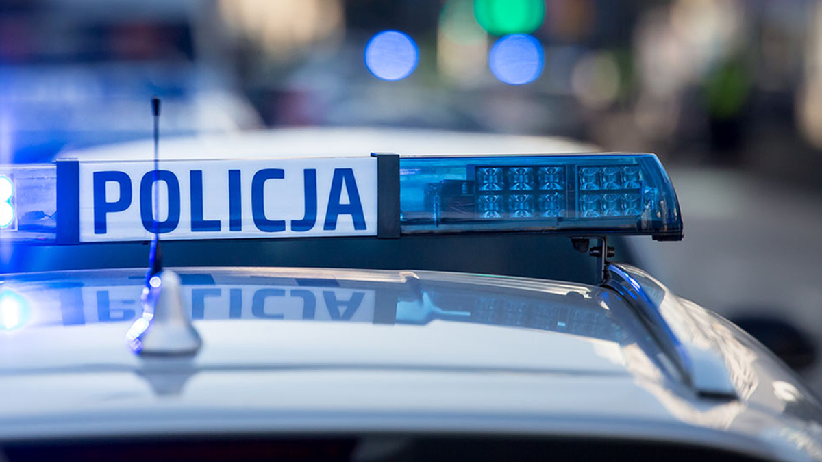 Radiow&oacute;z policyjny z włączonym niebieskim światłem sygnalizacyjnym i napisem POLICJA.