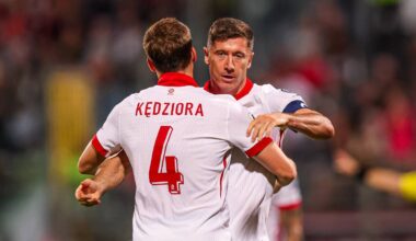 Dwóch piłkarzy reprezentacji Polski w białych koszulkach świętuje bramkę, jeden z nich, z numerem 4 i nazwiskiem KĘDZIORA, jest obejmowany przez drugiego.