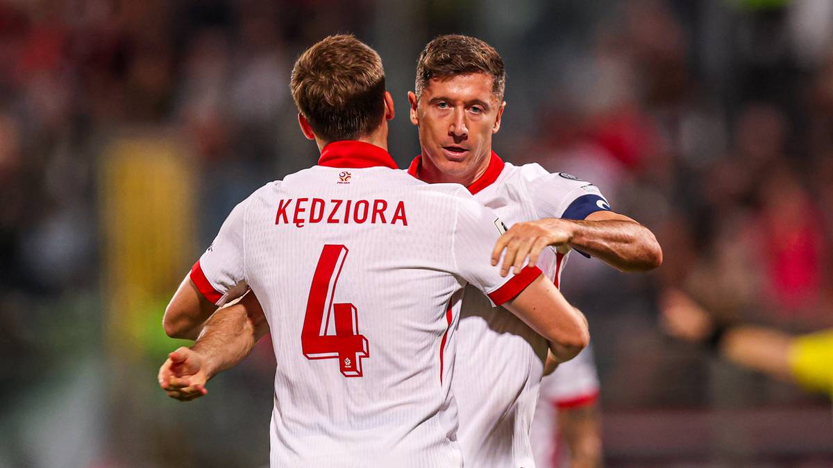 Dwóch piłkarzy reprezentacji Polski w białych koszulkach świętuje bramkę, jeden z nich, z numerem 4 i nazwiskiem KĘDZIORA, jest obejmowany przez drugiego.