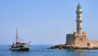 Żaglowiec płynie po morzu w pobliżu kamiennej latarni morskiej na wyspie.