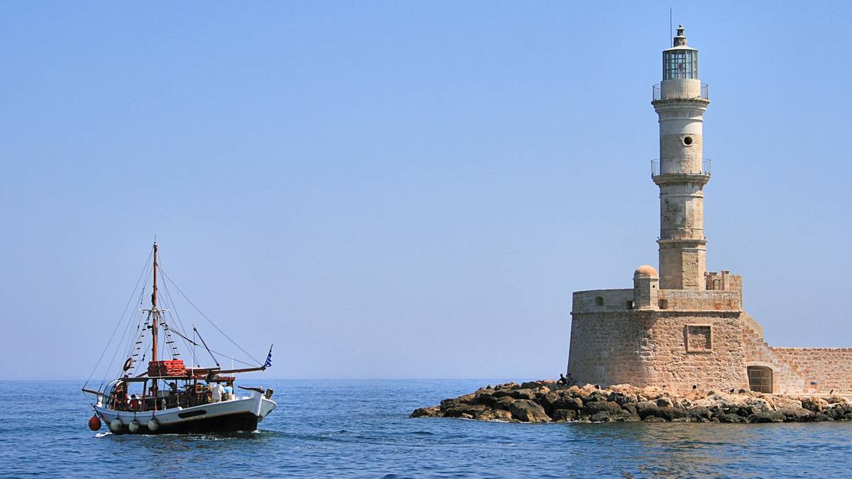 Żaglowiec płynie po morzu w pobliżu kamiennej latarni morskiej na wyspie.