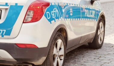 Tylna część białego samochodu policyjnego z niebieskimi pasami i napisem "POLICJA"