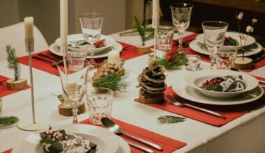 Ustawiony na biały obrus st&oacute;ł wigilijny z czerwonymi podkładkami i ozdobami.