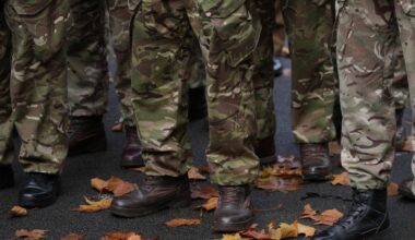 Zbliżenie na nogi żołnierzy w mundurach kamuflażowych i butach wojskowych, stojących na ziemi pokrytej opadłymi liśćmi.
