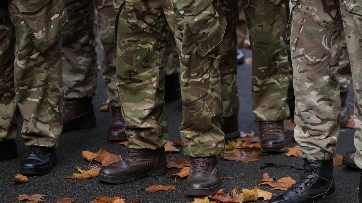 Zbliżenie na nogi żołnierzy w mundurach kamuflażowych i butach wojskowych, stojących na ziemi pokrytej opadłymi liśćmi.