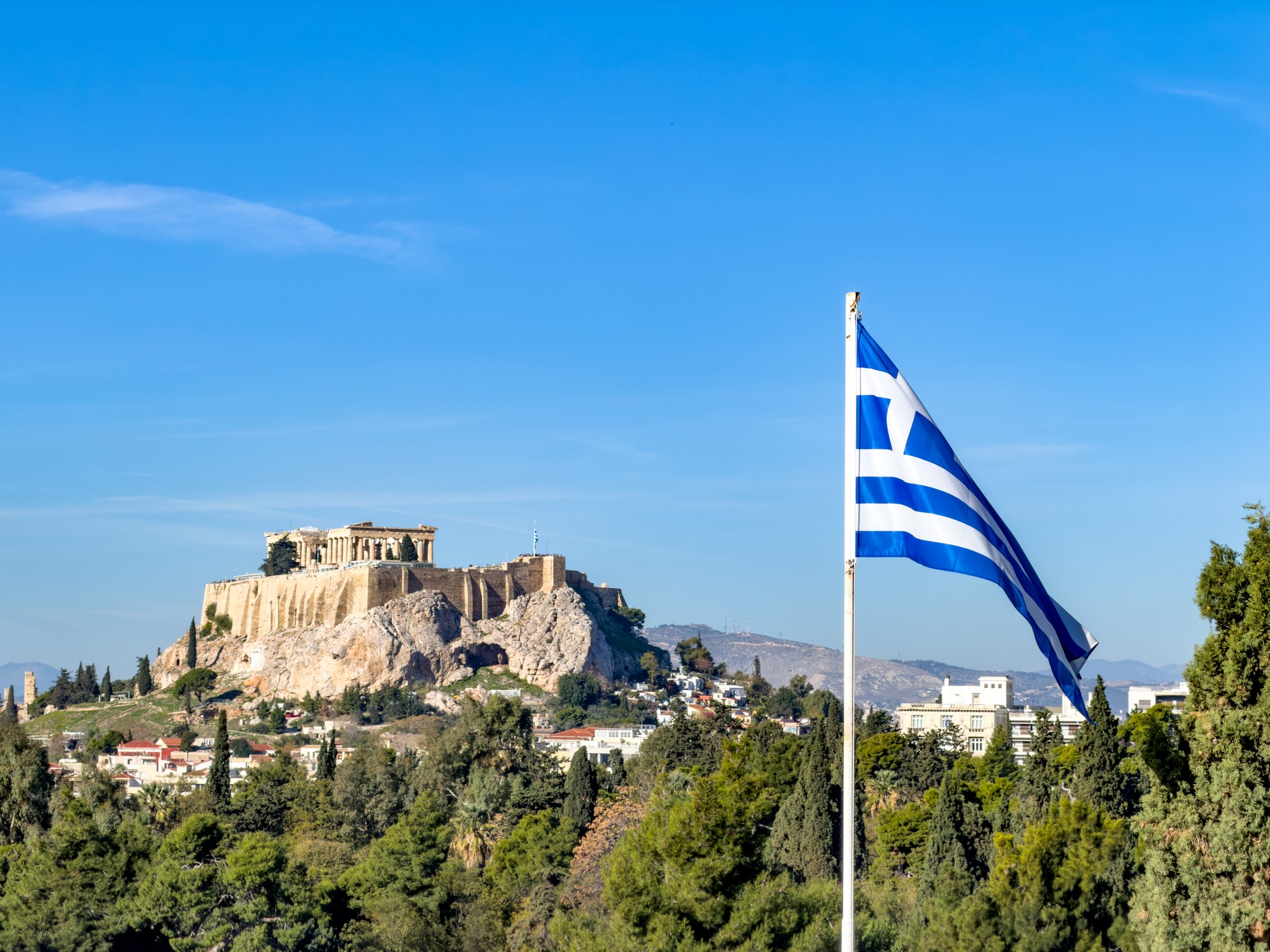 Flaga grecka powiewająca obok wzgórza Akropolu w Atenach