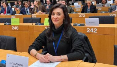 Kobieta siedzi przy stole w sali konferencyjnej, przed nią leżą dokumenty i identyfikator z napisem "EWA ZAJĄCZKOWSKA-HERNIK"