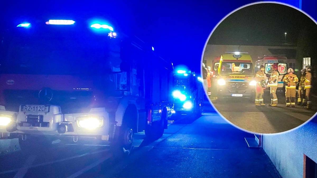 Straż pożarna i pogotowie ratunkowe na miejscu zdarzenia w nocy, z zapalonymi niebieskimi światłami.