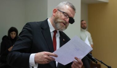 Grzegorz Braun w garniturze i z opaską na oku, trzymający dokumenty.