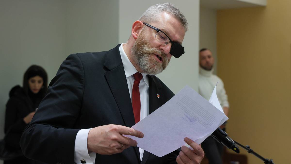 Grzegorz Braun w garniturze i z opaską na oku, trzymający dokumenty.