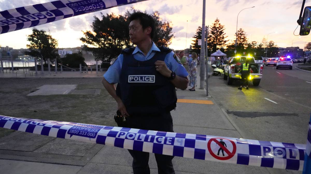 Policjant w kamizelce "POLICE" stoi za taśmą policyjną.
