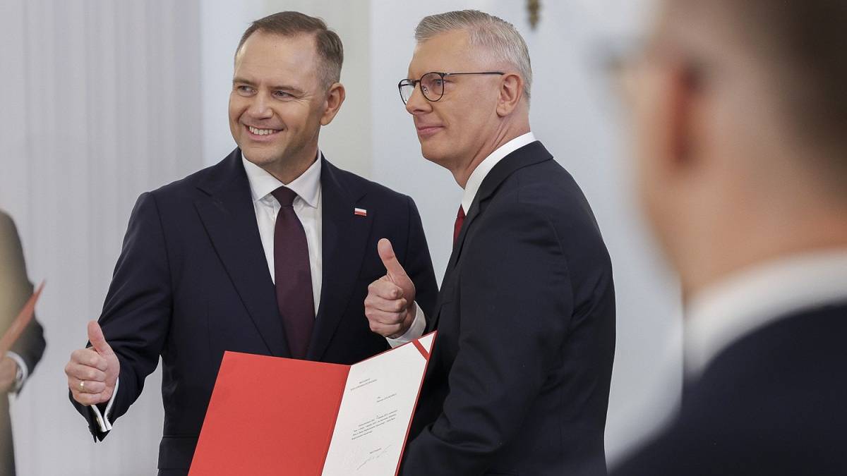 Dw&oacute;ch mężczyzn w garniturach, jeden z nich uśmiecha się i pokazuje kciuk w g&oacute;rę, trzymając czerwony folder.