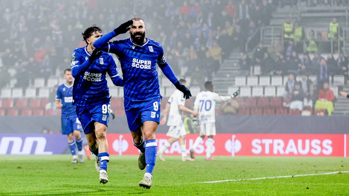 Piłkarze w niebieskich strojach świętują zdobycie bramki na zielonej murawie stadionu, z trybunami pełnymi kibic&oacute;w w tle.