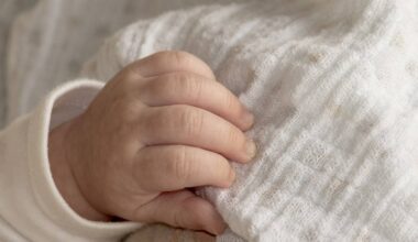 Dłoń niemowlęcia owinięta w biały, wzorzysty materiał.