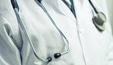 Zbliżenie na biały fartuch lekarski z wetkniętym stetoskopem na klatce piersiowej.