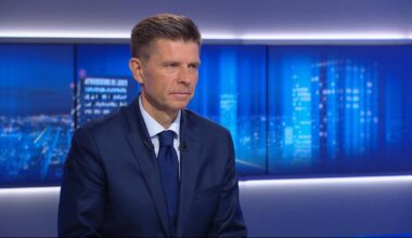 Mężczyzna w granatowym garniturze i białej koszuli z niebieskim krawatem, patrzący przed siebie.