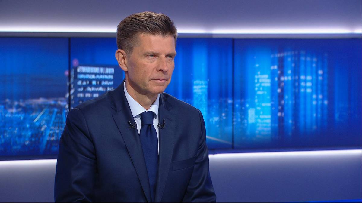 Mężczyzna w granatowym garniturze i białej koszuli z niebieskim krawatem, patrzący przed siebie.