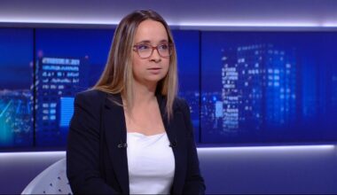 Kobieta w okularach i marynarce siedzi w studiu telewizyjnym.